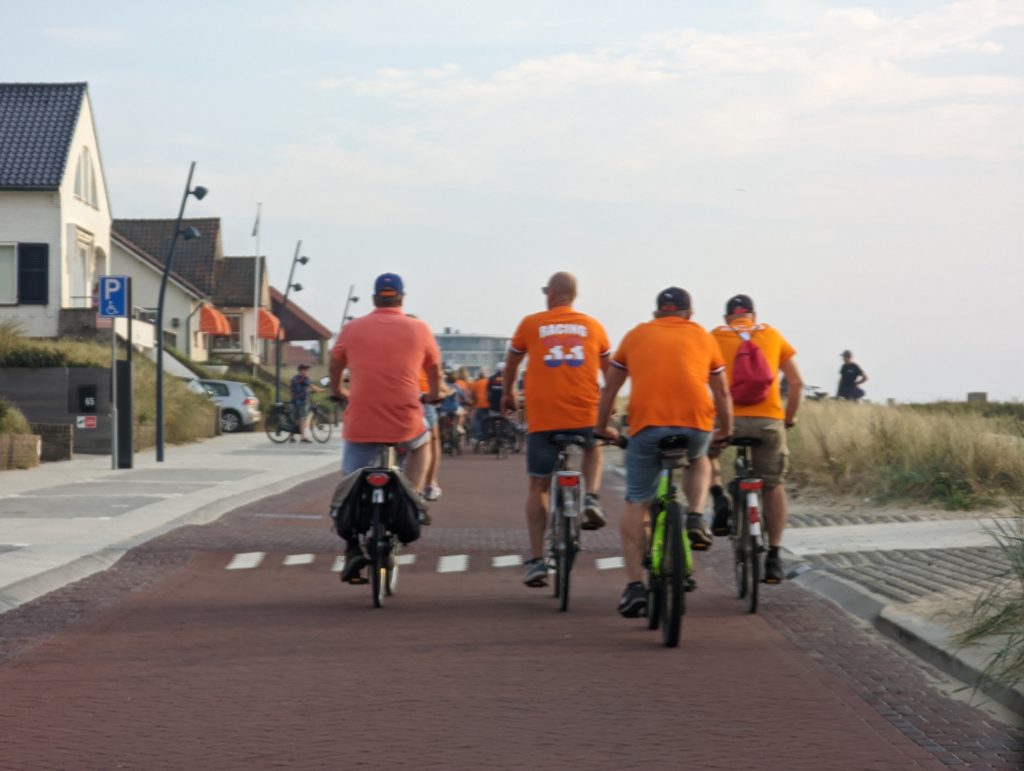 4 Radfahrer mit orangen T-Shirts auf einem breiten Radweg