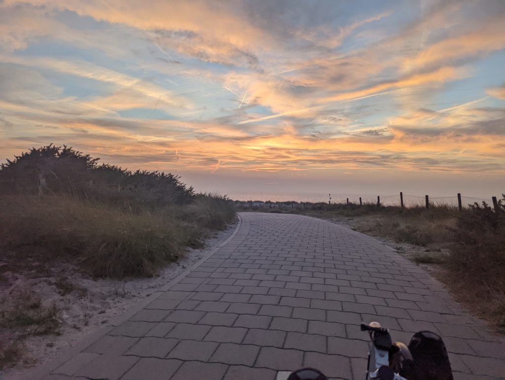 Ein gepflasterter Radweg in den Dünen bei Sonnenuntergang